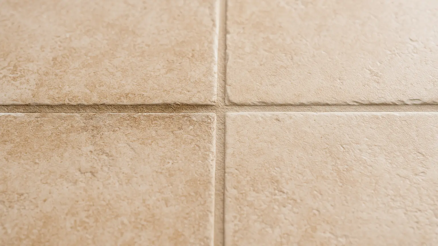Close-up of grout lines between floor tiles showing uneven wear patterns in high-traffic pathways, with sealed and unsealed sections visible side by side.